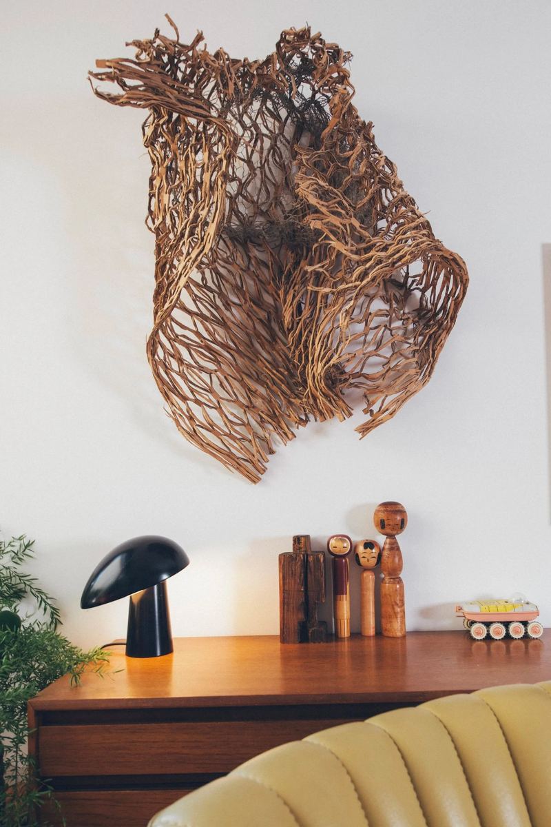 Wandskulptur aus Wurzelgeflecht über einem Teakholz-Sideboard mit schwarzer Pilzleuchte und Holzfiguren