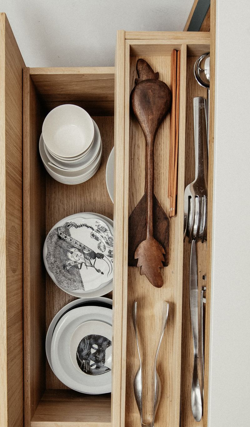 Geöffneter Tablarschrank mit Tellern und Holzlöffeln in schmalen Fächern