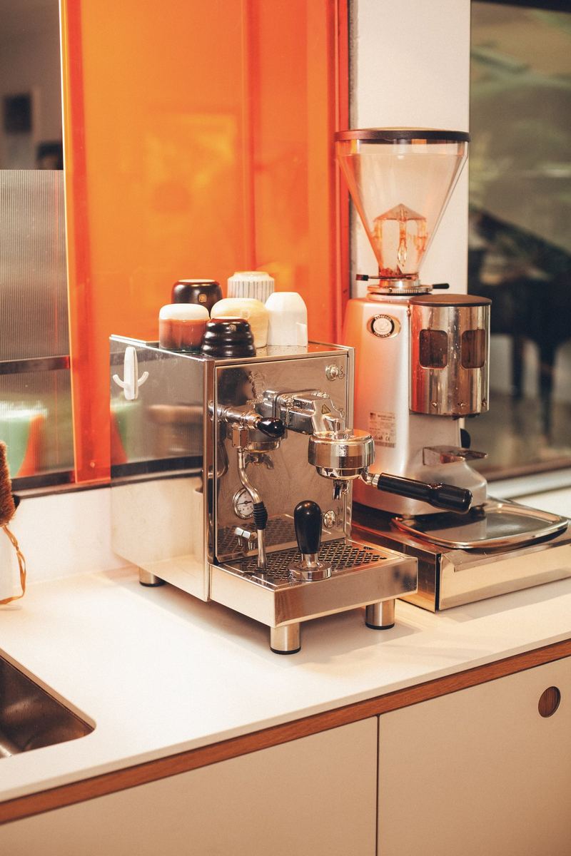 Siebträgermaschine und Mühle vor einer orangefarbenen Glaswand