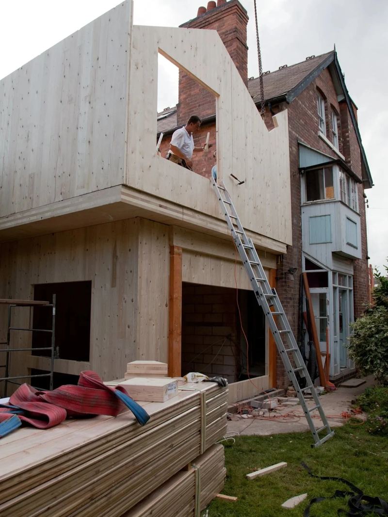 Holzrohbau mit Leiter, im Vordergrund gestapelte Bauteile