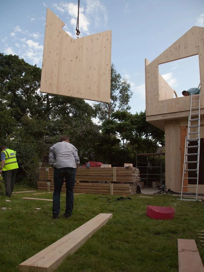 Ein Wandelement aus Holz schwebt am Kran über dem Garten