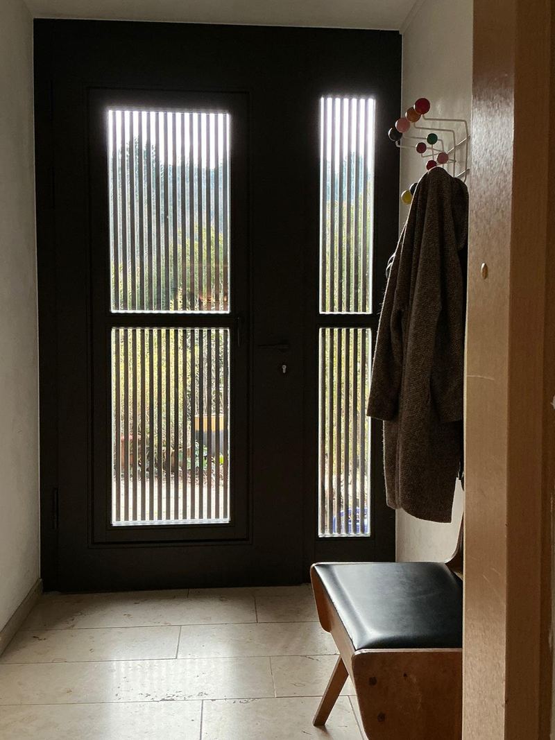 Die neue Tür von innen: Glas mit Lamellen, daneben Garderobe und Bank