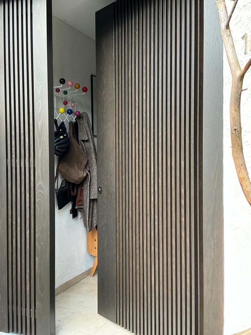 Geöffnetes Türblatt mit Lamellen, dahinter Garderobe